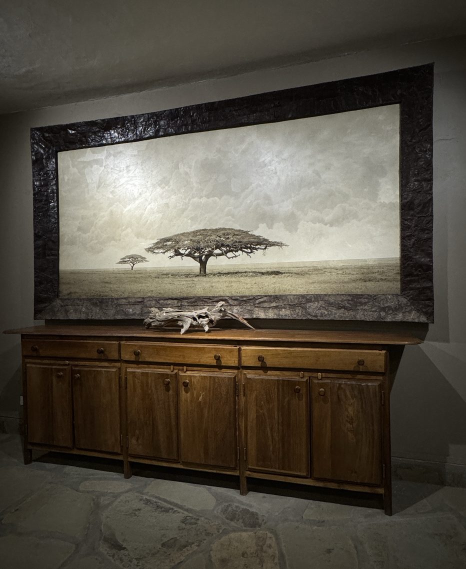 Wide acacia landscape in a carved dark frame above a wooden sideboard