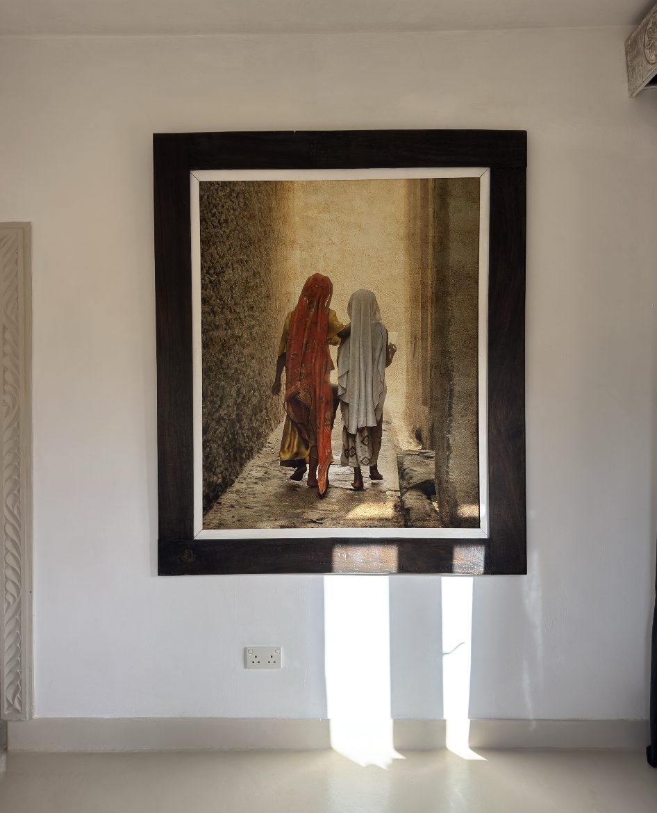 Two women walking in an alley, framed on a white wall
