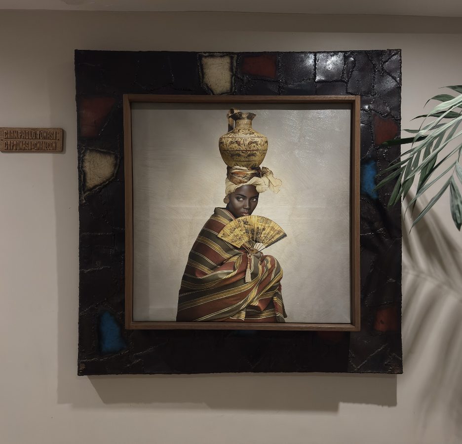 Woman with a jug on her head and a fan, in a wide dark frame
