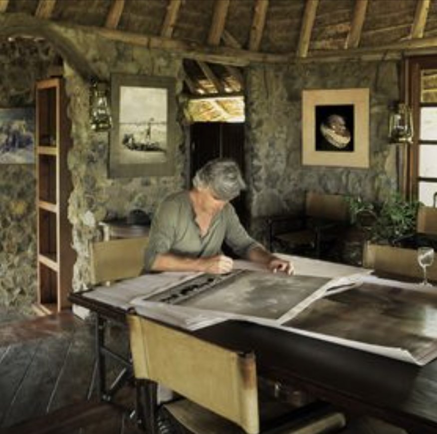 Gian Paolo Tomasi at a wooden table reviewing large prints in a stone and thatch studio
